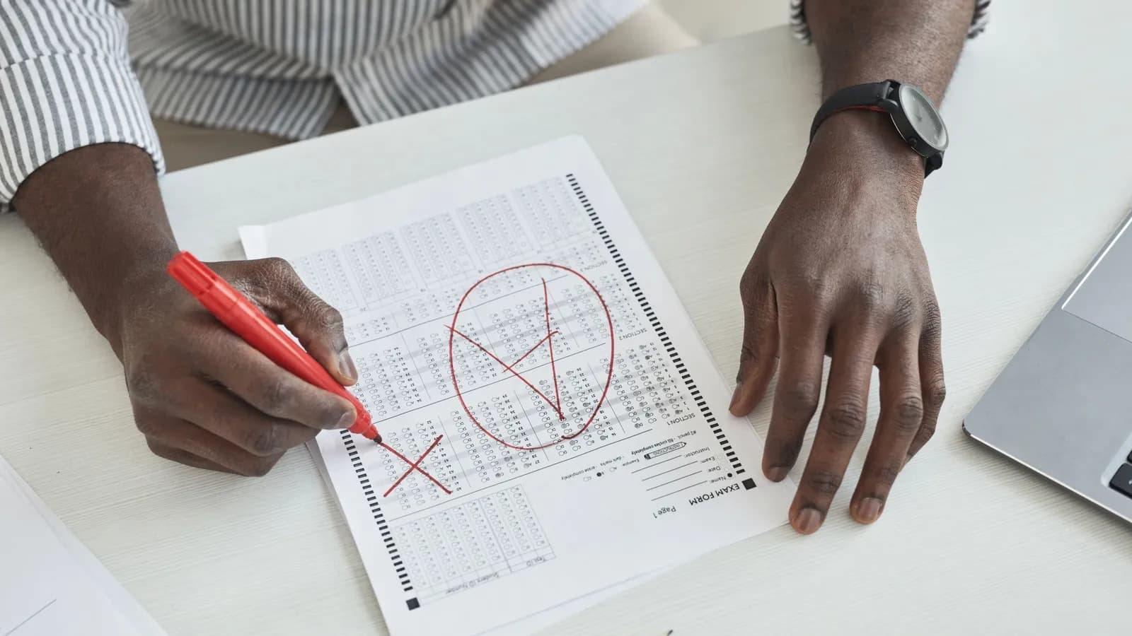 A close-up of a hand marking a test paper with a red pen.