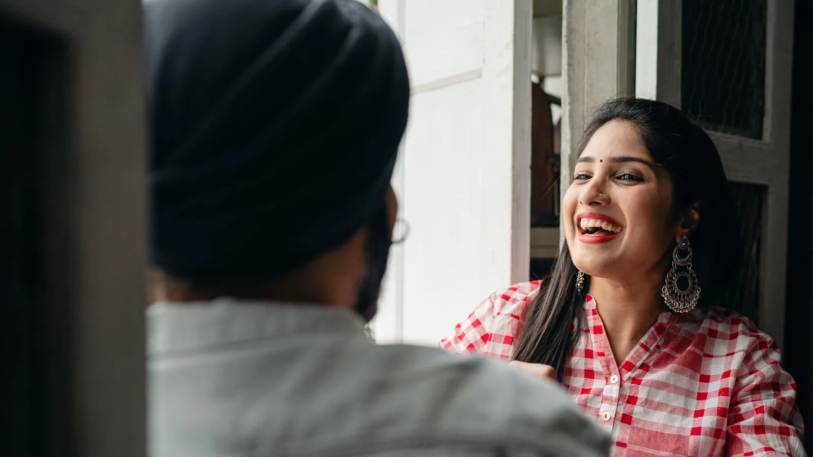 A young Indian woman in a checked shirt laughs while talking with a man in a turban.