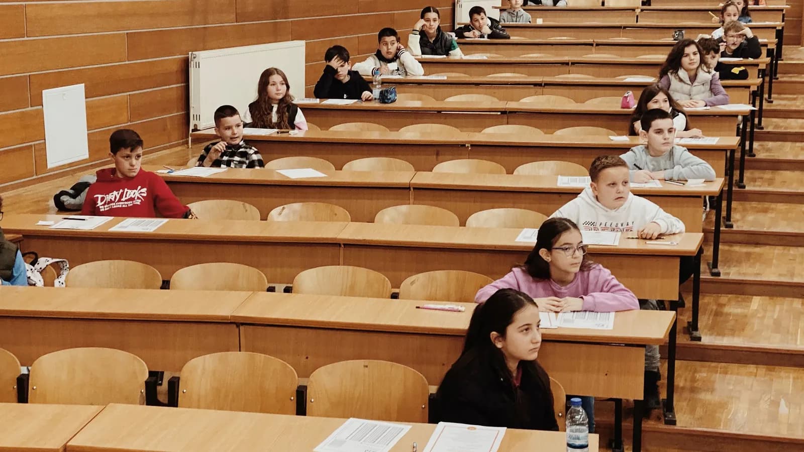 Students sit spaced out in rows in a lecture hall, writing an exam.